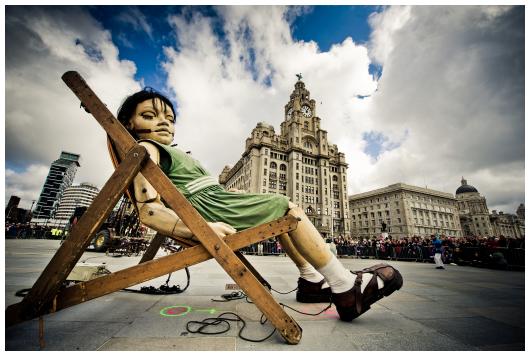 Image of the Little Giant Girl sitting in a deckchair asleep in front of the Liver Birds